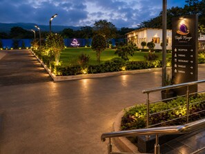 A hotel entrance with a reception sign, directional arrows for amenities, and a well-lit pathway leading to the building. - The Purple Mango - Pure Veg (Lonavala)