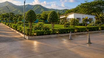 A paved pathway leading to a building with a landscaped garden and a mountain in the background.