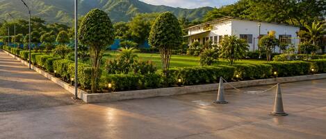 A paved pathway leading to a building with a landscaped garden and a mountain in the background.