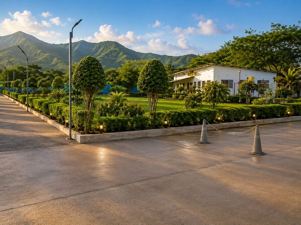 A paved pathway leading to a building with a landscaped garden and a mountain in the background.