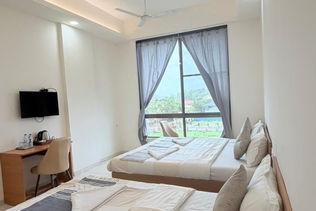 A hotel room with a bed, a desk, a chair, a television, and a window with curtains.