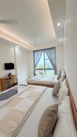 A hotel room with a bed, a desk, a chair, a television, and a window with curtains. - The Purple Mango - Pure Veg (Lonavala)