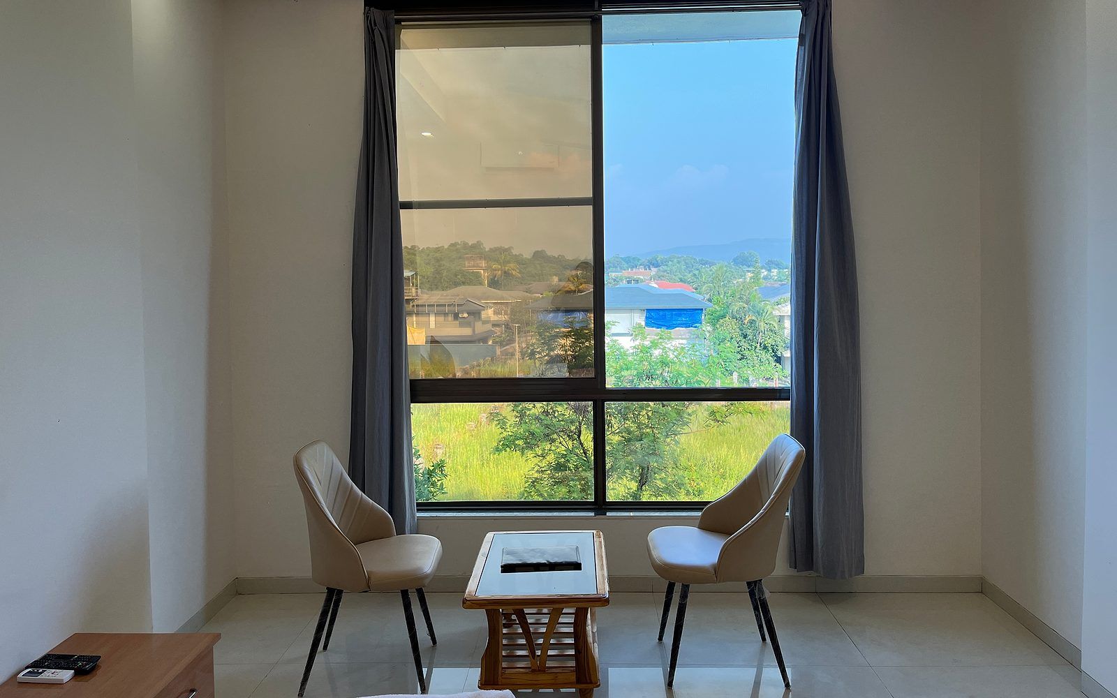 Ein Zimmer mit großem Fenster, zwei Stühlen, einem kleinen Tisch und Blick auf eine grüne Landschaft.