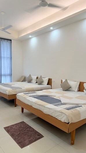 A hotel room with two single beds, a ceiling fan, and a window with curtains. - The Purple Mango  (Mawal)