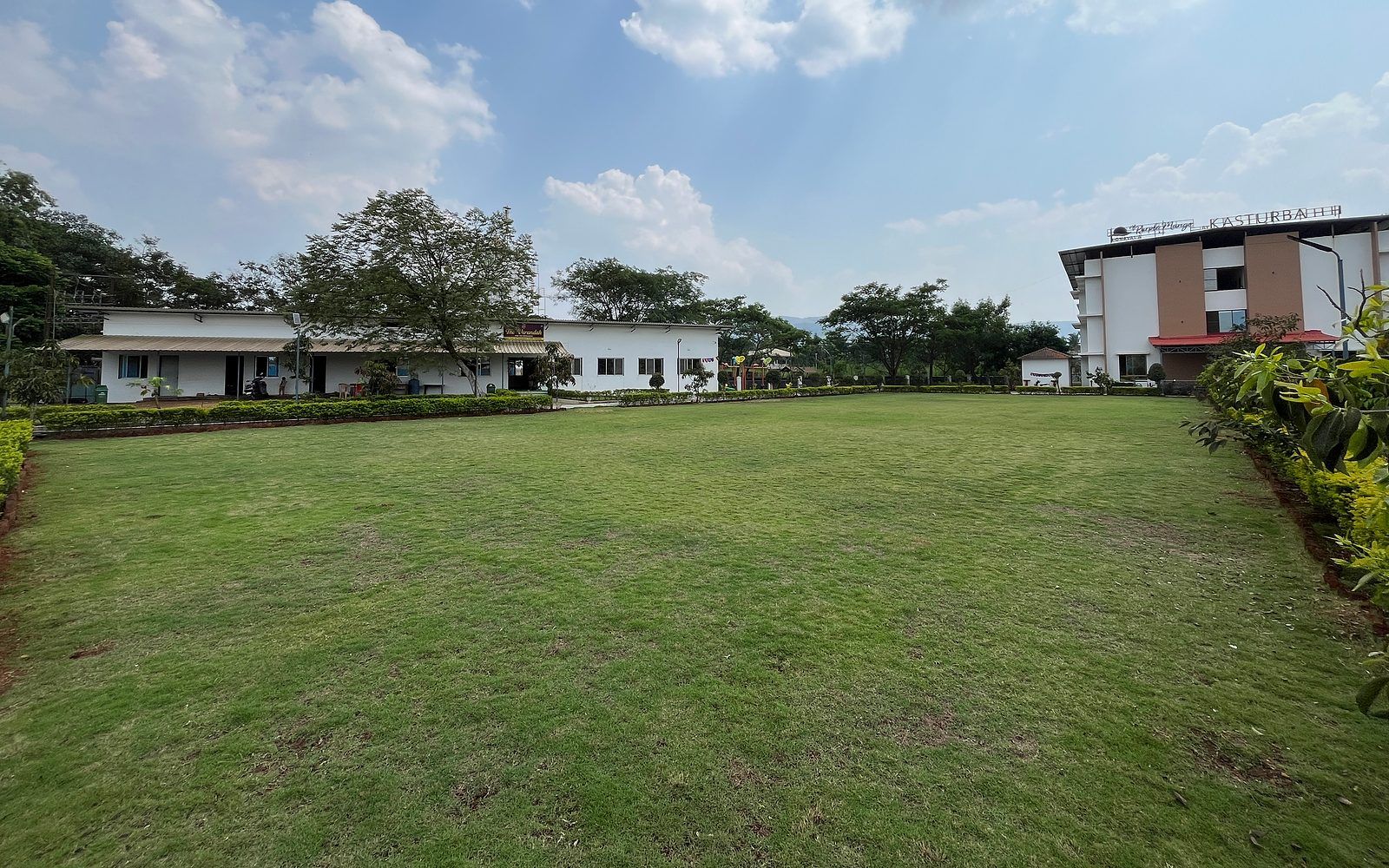 A grassy courtyard with buildings on either side, including a hotel named 'Kasturbah.'