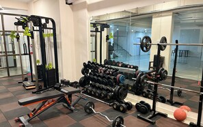 Academia com diversos equipamentos de musculação, incluindo halteres, barras e um banco.