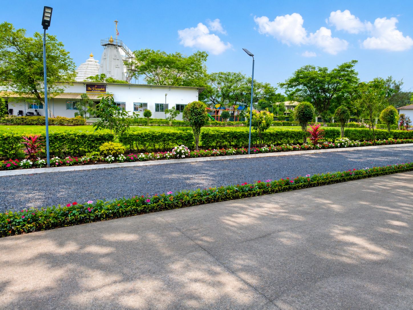 A well-maintained garden with a paved walkway, a white building with a dome, and a clear blue sky.