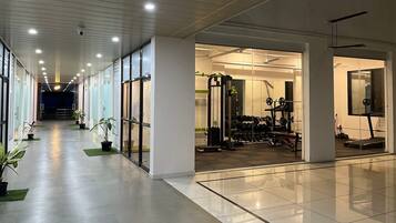 Un gimnasio con equipamiento de ejercicio, un pasillo con plantas en macetas e iluminación empotrada en el techo.