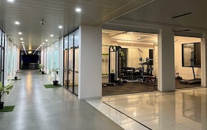 A gym with exercise equipment, a corridor with potted plants, and a ceiling with recessed lighting. - The Purple Mango - Pure Veg (Lonavala)
