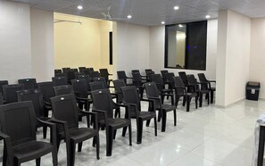 A conference room with rows of black chairs, a projector screen, and a ceiling fan. - The Purple Mango - Pure Veg (Lonavala)