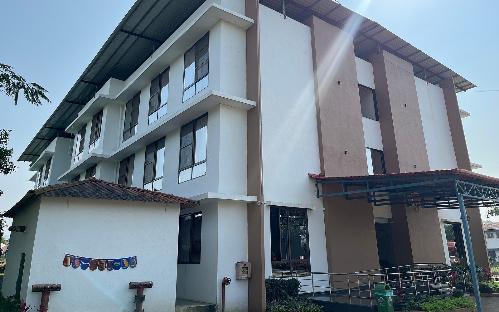 Um edifício com vários andares, teto plano, entrada coberta e uma pequena área ajardinada.