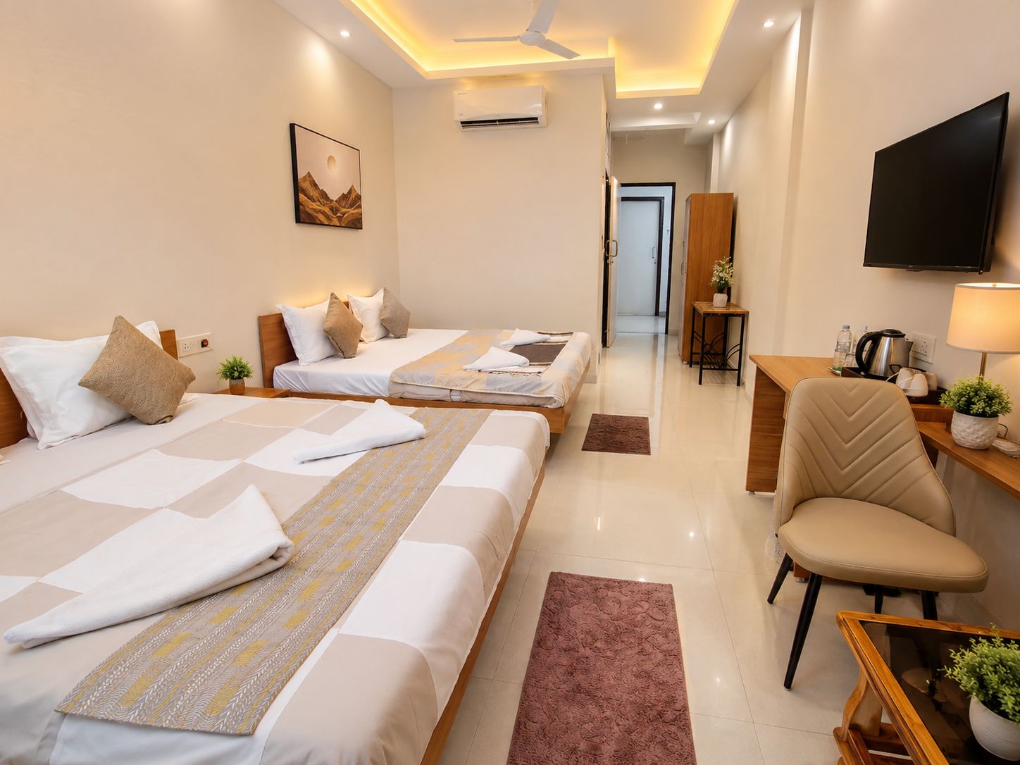 Une chambre d’hôtel avec deux lits, un bureau, une chaise, une télévision et un ventilateur de plafond.