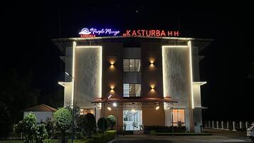 A hotel with a prominent sign reading 'Purple Mango' and 'Kasturba HH' at night.
