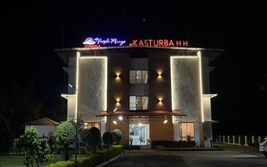 Um hotel com uma placa de destaque que diz 'Purple Mango' e 'Kasturba HH' à noite.
