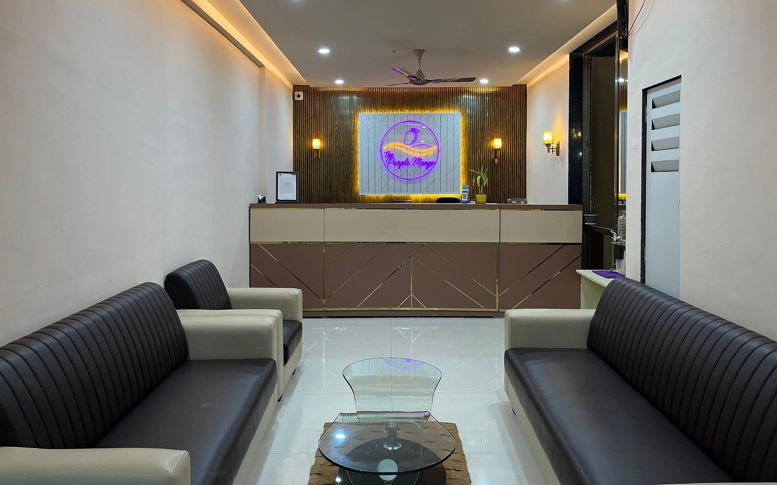 A reception area with a reception desk, two sofas, a glass coffee table, and a ceiling fan.