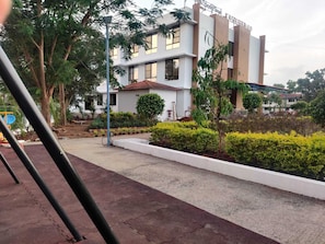 Un edificio de varios pisos con fachada blanca, rodeado de vegetación y un sendero pavimentado.