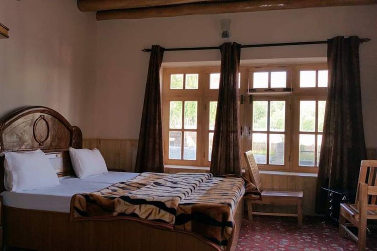 A bedroom with a wooden bed, a wooden nightstand, a chair, and a window with curtains.