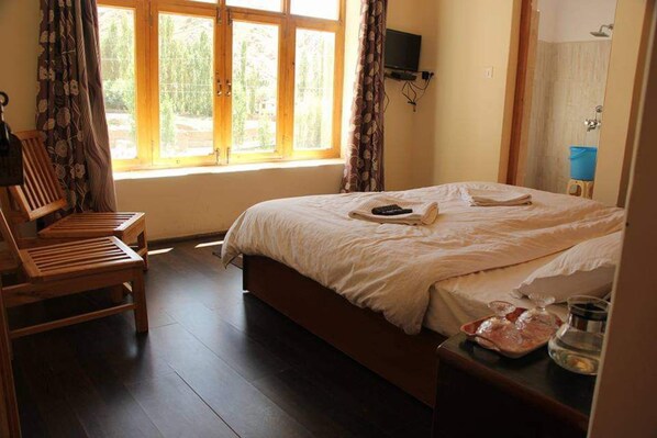 Un dormitorio con una cama grande, sillas de madera, un televisor y una ventana.