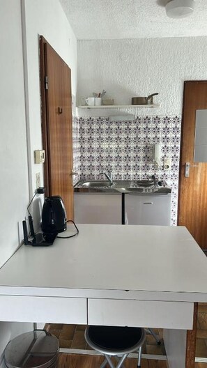 Ett kompakt kök med en vit bänkskiva, en diskho och mönstrade kakelplattor ovanför.