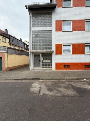 En byggnad med flera våningar, vars fasad består av en blandning av tegel och kakel, med en tydligt markerad entré i bottenvåningen och en klar himmel i bakgrunden.
