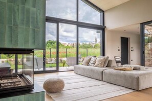 Een moderne woonkamer met een groot raam, een open haard, een hoekbank en een stenen muur.