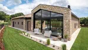 A modern house with a stone facade, large glass windows, and a patio with outdoor furniture. - Villa Casa di Nova (Bale)