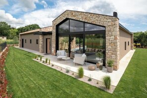 A modern house with a stone facade, large glass windows, and a patio with outdoor furniture. - Villa Casa di Nova (Bale)