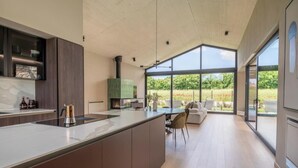 A modern kitchen with a large island, a dining area with a sofa, and large windows offering a view of the outdoors. - Villa Casa di Nova (Bale)