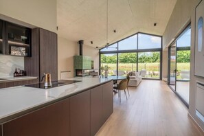A modern kitchen with a large island, a dining area with a sofa, and large windows offering a view of the outdoors. - Villa Casa di Nova (Bale)