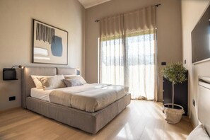 A bedroom with a bed, a potted plant, a wall-mounted TV, and a window with curtains. - Villa Casa di Nova (Bale)