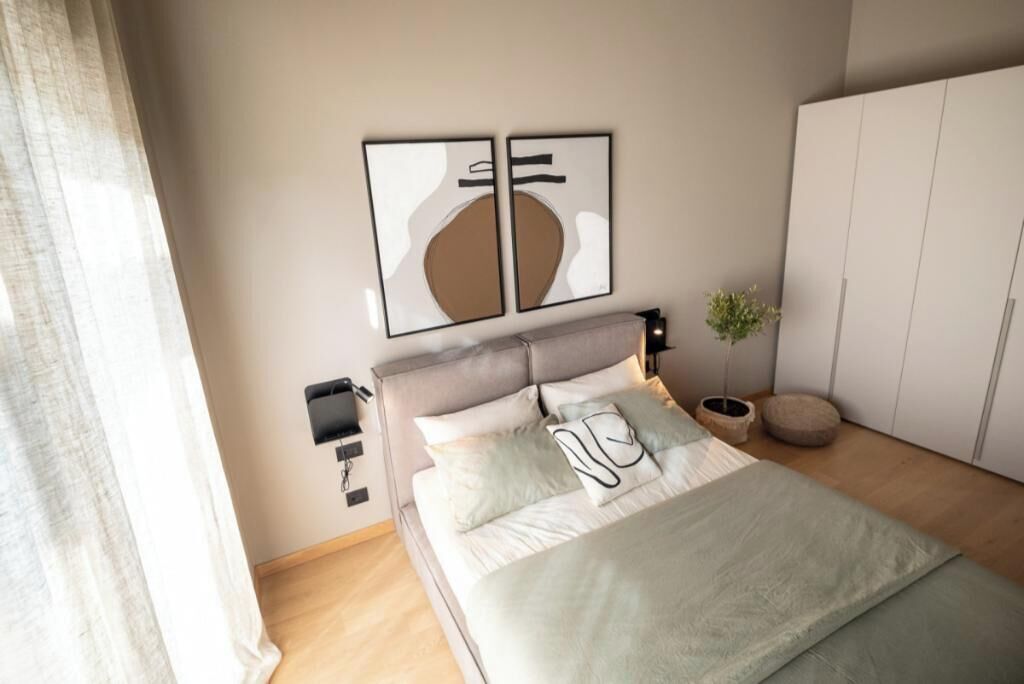 A modern bedroom with a bed, bedside tables, a nightstand, and a wall-mounted light fixture.