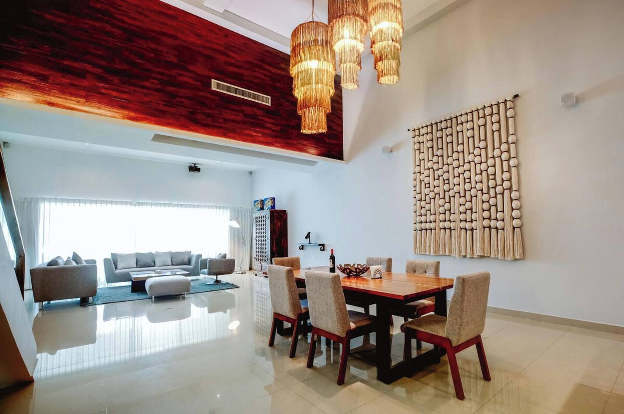 A modern living room with a dining area, a chandelier, and a textured wall art piece.