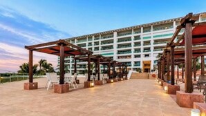Un hotel con una zona de estar al aire libre techada, un edificio de varios pisos y un cielo despejado.