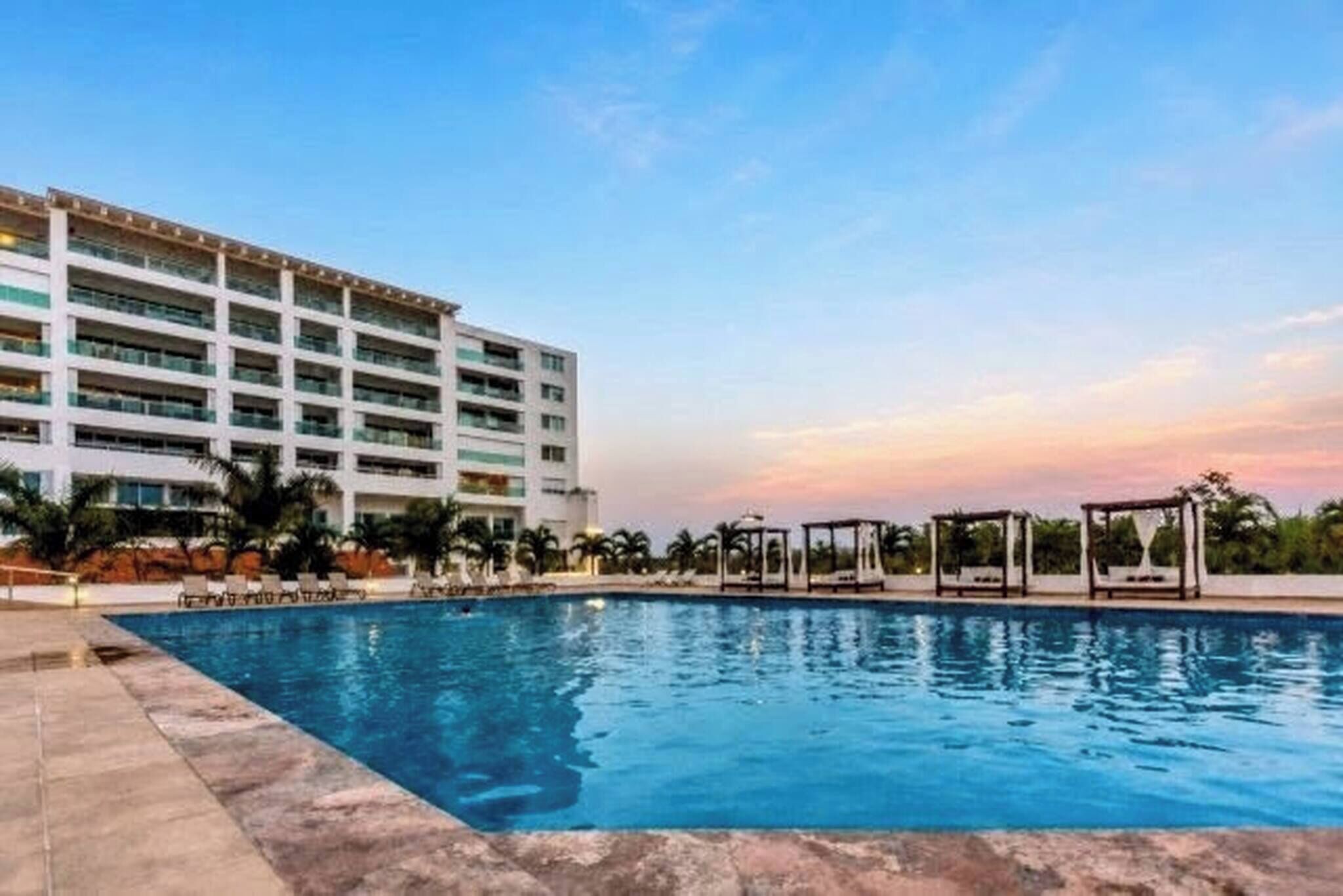 A hotel with a swimming pool, multiple floors, and a clear sky.