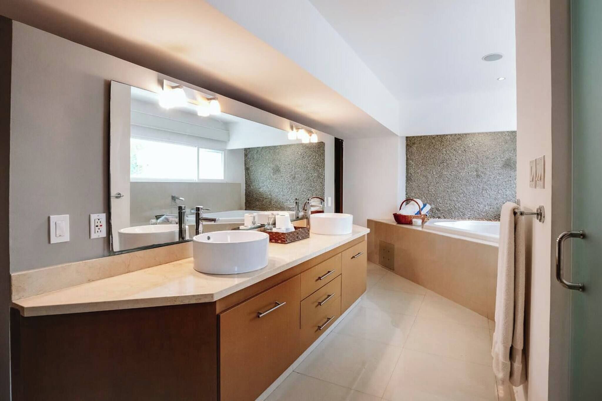 Ein modernes Badezimmer mit einem großen Spiegel, zwei Waschbecken, einer Badewanne und einem Handtuchhalter.