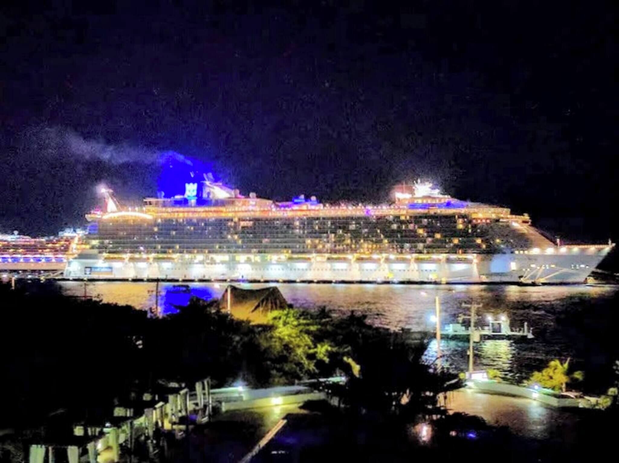 Een groot cruiseschip in de haven, verlicht met felle lampen over meerdere dekken.