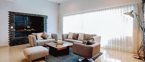 A modern living room with a sectional sofa, a coffee table, and a flat-screen TV mounted on a stone wall.