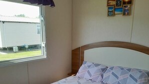 A single bed with a geometric patterned bedspread, a window with a view of a building outside, and a wall with framed pictures. - Ty Mawr Holiday Park - Holiday Accommodation 21752 (Abergele)