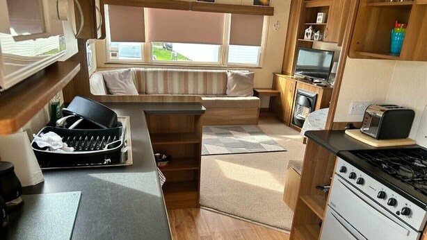 A compact kitchen with a stove, sink, and a small dining area with a bench. - Ty Mawr Holiday Park - Holiday Accommodation 21752 (Abergele)