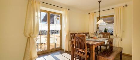 A dining area with a wooden table and chairs, a chandelier, and a view through a glass door.