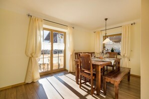 Zona pranzo con tavolo e sedie in legno, un lampadario e vista attraverso una porta in vetro.