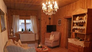 En ombonad träinredning med en kristallkrona, en mönstrad fåtölj, en tv och ett litet julgran.