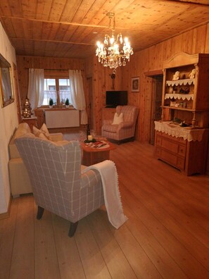 Un ambiente accogliente in legno, con un lampadario, una poltrona a quadri, un televisore e un piccolo abete di Natale.