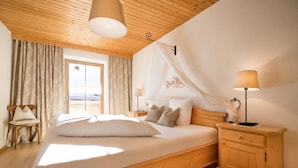 Ein Schlafzimmer mit einem hölzernen Bett, einem Nachttisch, einer Lampe, einem Stuhl und einem Fenster mit Vorhängen.