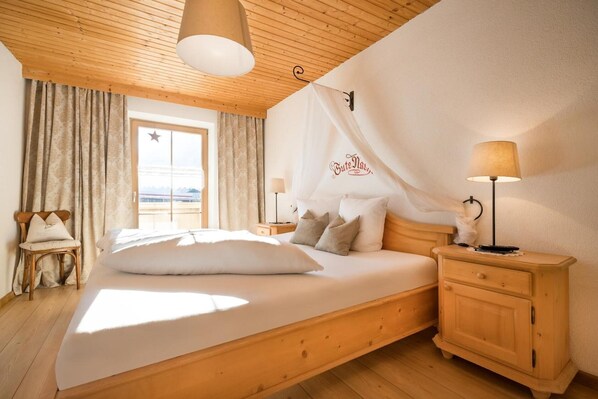 A bedroom with a wooden bed, a nightstand, a lamp, a chair, and a window with curtains.