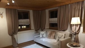 Ein gemütliches Wohnzimmer mit einer Couch, einem runden Tisch und zwei mit Vorhängen versehenen Fenstern.