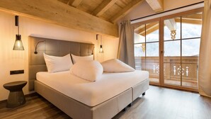 Ein Schlafzimmer mit einem Bett, Nachttischlampen, einer Holzbalkendecke und einer Schiebetür zu einem Balkon.