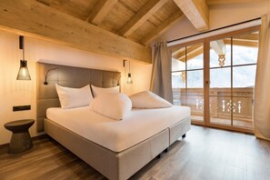 Quarto com cama, abajures, teto de madeira e porta de vidro deslizante para uma varanda.