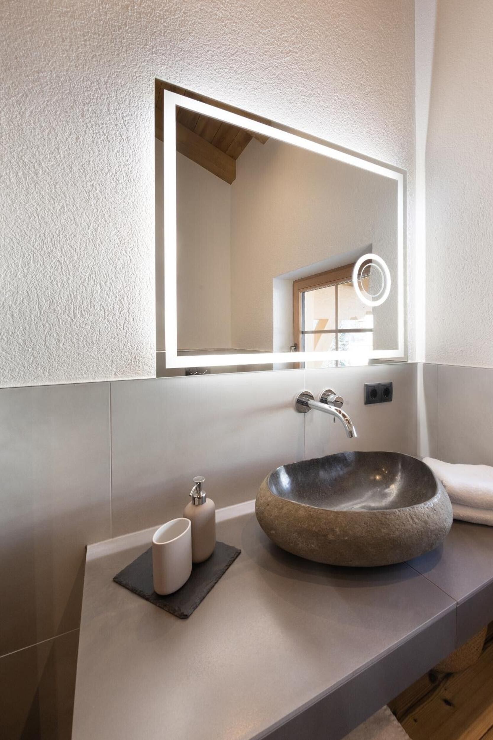 Ein modernes Badezimmer mit einem Becken aus Stein, einem Spiegel und einem kleinen Fenster.