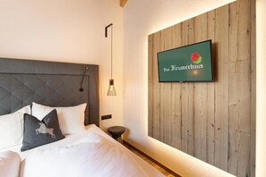 A hotel room with a bed, a TV mounted on a wooden wall, and a small stool.